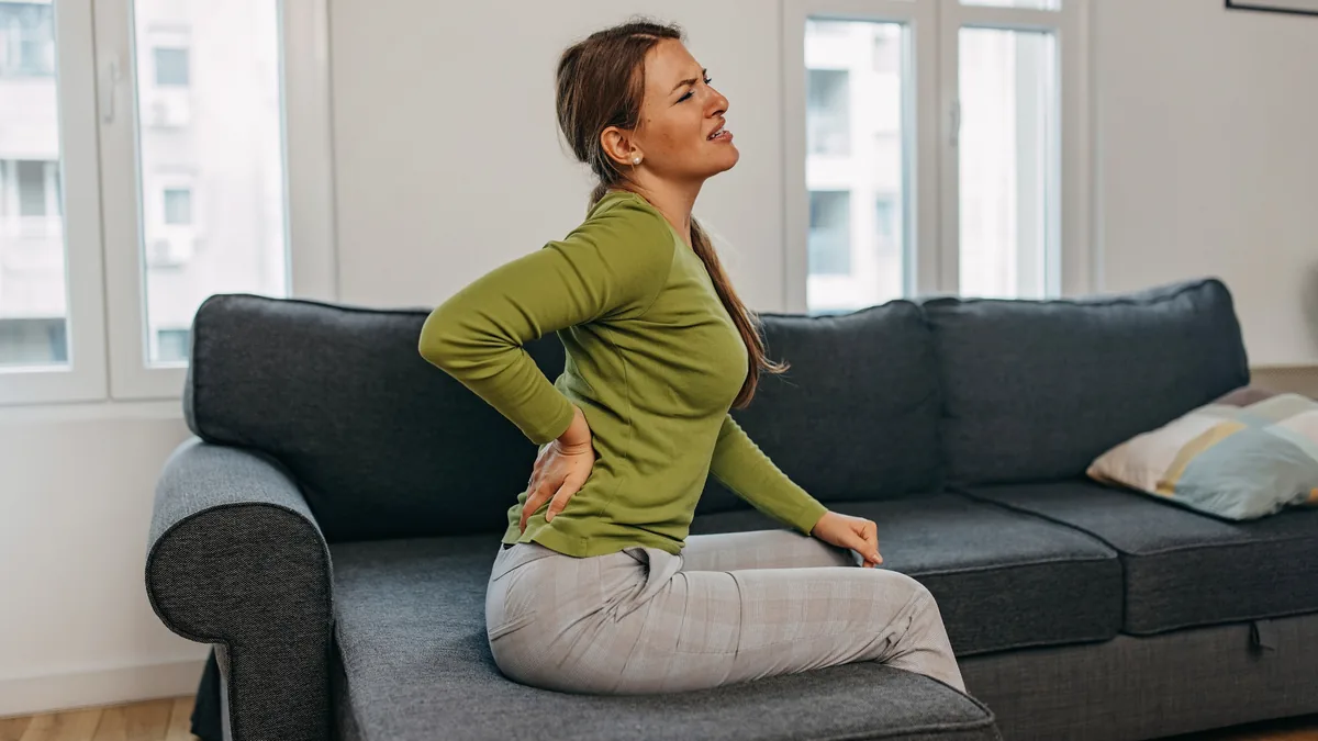 Frau auf dem Sofa hält sich den Rücken