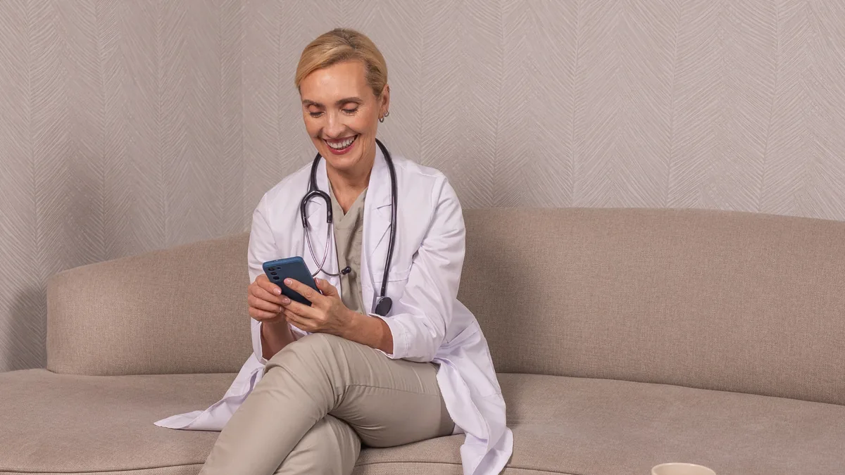 Ärztin sitzt lächelnd mit Smartphone auf dem Sofa