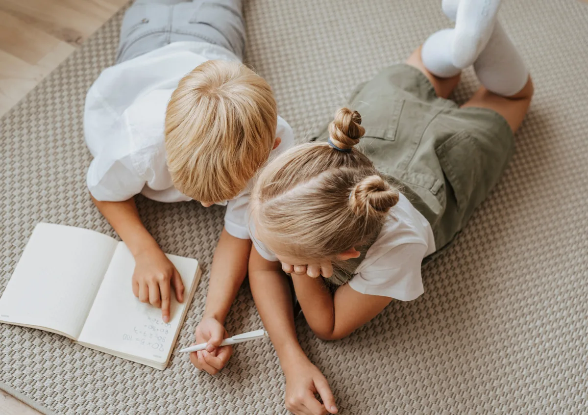 Zwei Kinder liegen auf dem Boden und malen